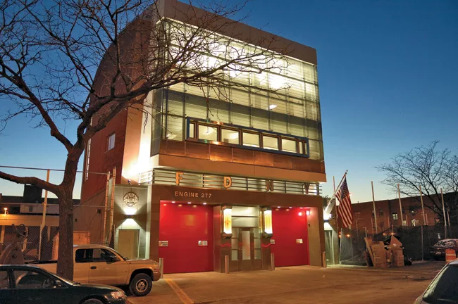The architects enclosed the upper two floors of this Brooklyn station in glass, while red doors open on the ground floor, creating a street-facing facade that reads as both a contemporary facility and
