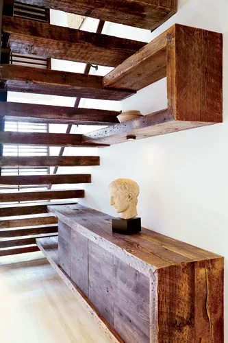 In keeping with her material scheme, Reddy designed a credenza and wall shelf to align with the stairs. Made out of the same reclaimed wood, these functional elements appear to float from the treads a
