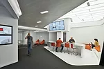 Five different &ldquo;hubs,&rdquo; each coded by a particular color, offer unprogrammed spaces for people to meet or relax. Overhead monitors and screens embedded in the work surfaces keep employees i