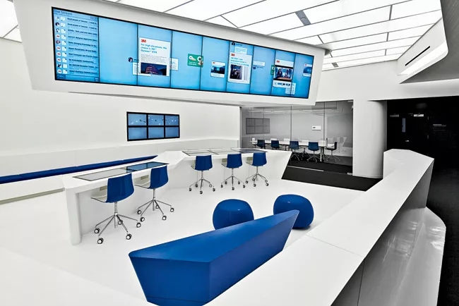 Five different “hubs,” each coded by a particular color, offer unprogrammed spaces for people to meet or relax. Overhead monitors and screens embedded in the work surfaces keep employees i
