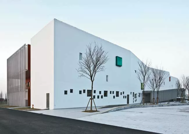 In the kindergarten, two parallel structures play in opposition to each other. A formidable concrete block encloses the circulation ramps for the school, while a punctured block with perforated alumin