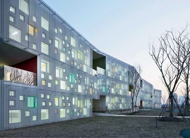 In the kindergarten, two parallel structures play in opposition to each other. A formidable concrete block encloses the circulation ramps for the school, while a punctured block with perforated alumin