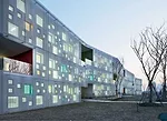 In the kindergarten, two parallel structures play in opposition to each other. A formidable concrete block encloses the circulation ramps for the school, while a punctured block with perforated alumin