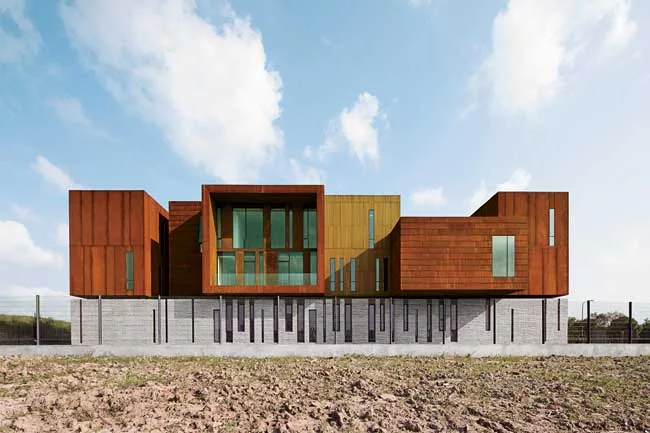 Surrounded by roads and vacant lots on three sides, the site for this building has just one notable feature: A river that runs along its north side. On its short sides, the building appears as a pair 