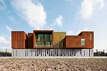Surrounded by roads and vacant lots on three sides, the site for this building has just one notable feature: A river that runs along its north side. On its short sides, the building appears as a pair 