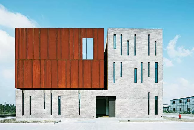 Surrounded by roads and vacant lots on three sides, the site for this building has just one notable feature: A river that runs along its north side. On its short sides, the building appears as a pair 