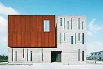 Surrounded by roads and vacant lots on three sides, the site for this building has just one notable feature: A river that runs along its north side. On its short sides, the building appears as a pair 