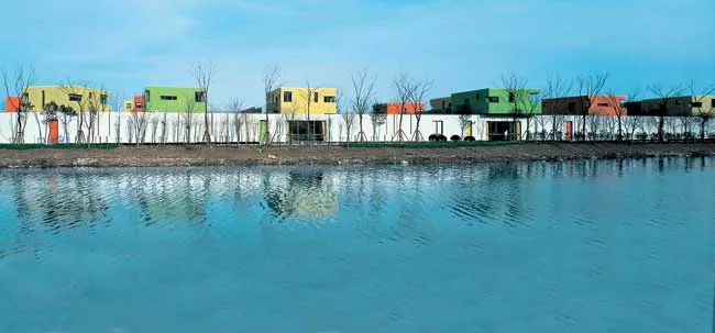 Fifteen classrooms, dining rooms, and courtyard play spaces nestle together in a long white band that follows the curve of an adjacent river. Fifteen corresponding nap rooms painted in bright colors s