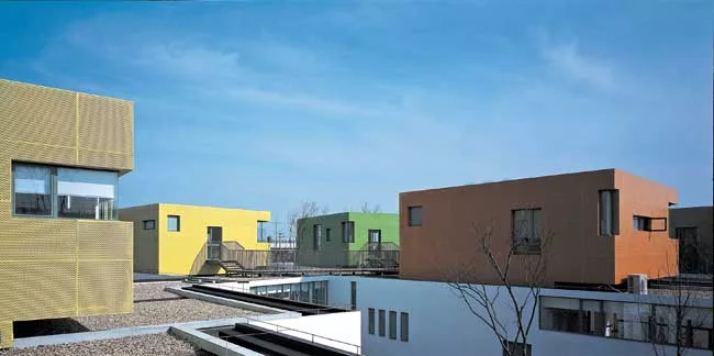 Fifteen classrooms, dining rooms, and courtyard play spaces nestle together in a long white band that follows the curve of an adjacent river. Fifteen corresponding nap rooms painted in bright colors s