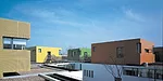 Fifteen classrooms, dining rooms, and courtyard play spaces nestle together in a long white band that follows the curve of an adjacent river. Fifteen corresponding nap rooms painted in bright colors s