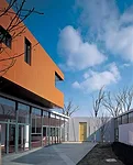 Fifteen classrooms, dining rooms, and courtyard play spaces nestle together in a long white band that follows the curve of an adjacent river. Fifteen corresponding nap rooms painted in bright colors s