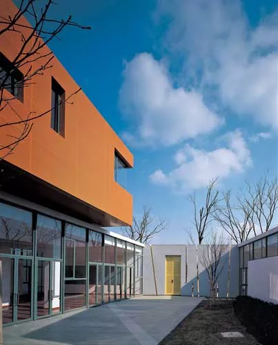 Fifteen classrooms, dining rooms, and courtyard play spaces nestle together in a long white band that follows the curve of an adjacent river. Fifteen corresponding nap rooms painted in bright colors s