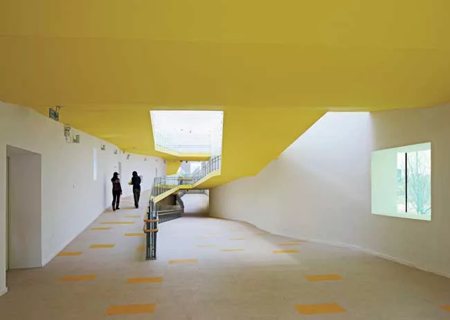 In the kindergarten, two parallel structures play in opposition to each other. A formidable concrete block encloses the circulation ramps for the school, while a punctured block with perforated alumin