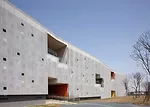 In the kindergarten, two parallel structures play in opposition to each other. A formidable concrete block encloses the circulation ramps for the school, while a punctured block with perforated alumin
