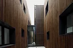 Surrounded by roads and vacant lots on three sides, the site for this building has just one notable feature: A river that runs along its north side. On its short sides, the building appears as a pair 