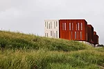 Surrounded by roads and vacant lots on three sides, the site for this building has just one notable feature: A river that runs along its north side. On its short sides, the building appears as a pair 