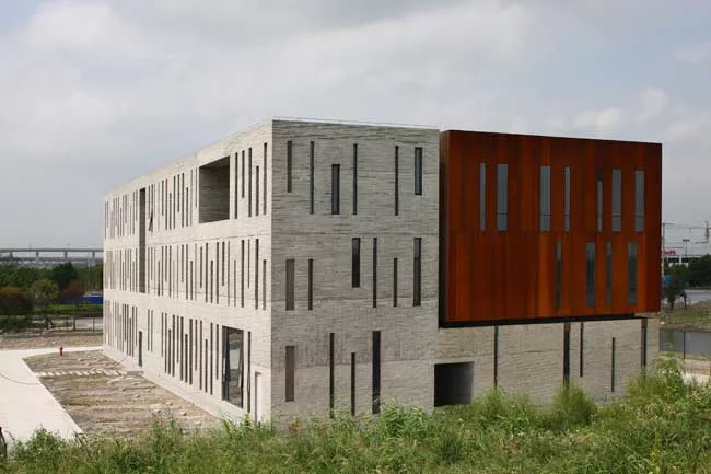 Surrounded by roads and vacant lots on three sides, the site for this building has just one notable feature: A river that runs along its north side. On its short sides, the building appears as a pair 