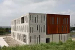 Surrounded by roads and vacant lots on three sides, the site for this building has just one notable feature: A river that runs along its north side. On its short sides, the building appears as a pair 