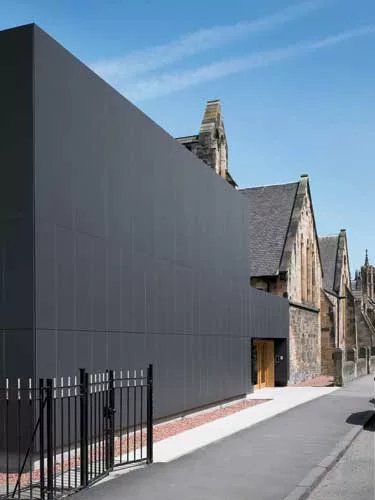 Asked to renovate an unremarkable 1970s annex to a church in Glasgow, the architects wrapped the building in black cement boards to provide a clear, flat contrast to the stone architecture next door.
