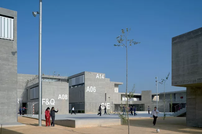 The 500-student school focuses inward around a small playing field, turning its back on the incomplete new development around it. Indoor and outdoor corridors circle the field and widen into courtyard