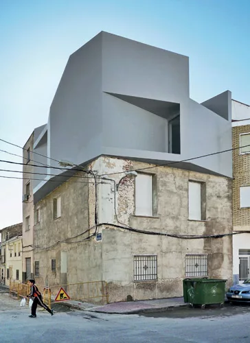 The client added a one-bedroom penthouse to the modest building where his mother and sister live. The architects oriented windows at oblique angles to the streets for views and protection from direct