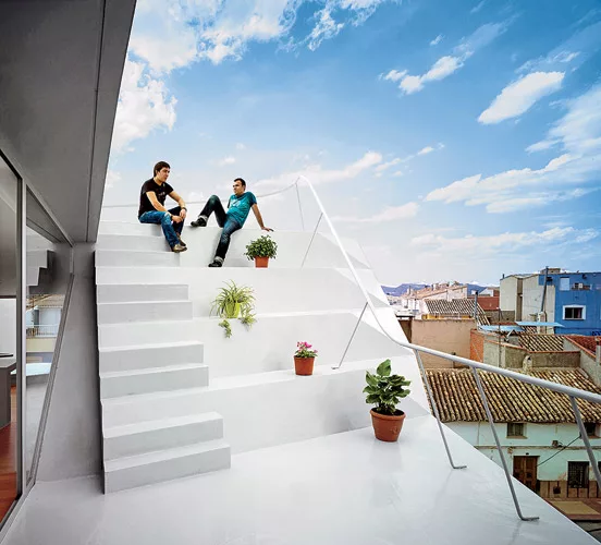 The client added a one-bedroom penthouse to the modest building where his mother and sister live. The architects oriented windows at oblique angles to the streets for views and protection from direct
