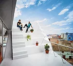 The client added a one-bedroom penthouse to the modest building where his mother and sister live. The architects oriented windows at oblique angles to the streets for views and protection from direct 