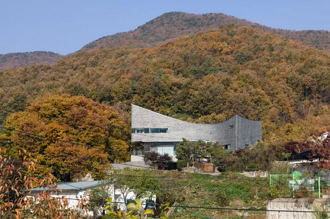The curve of this 1513-square-foot house has an unexpected origin'car parking. Its tight site made maneuvering vehicles difficult, so JOHO added a curve and raised the building on <em>pilotis</em>. Th