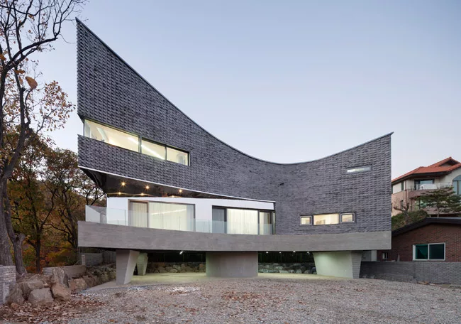 The curve of this 1513-square-foot house has an unexpected origin'car parking. Its tight site made maneuvering vehicles difficult, so JOHO added a curve and raised the building on <em>pilotis</em>. Th