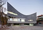The curve of this 1513-square-foot house has an unexpected origin'car parking. Its tight site made maneuvering vehicles difficult, so JOHO added a curve and raised the building on <em>pilotis</em>. Th