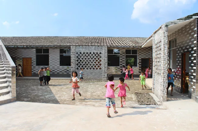 With this six-classroom addition to a primary school in Jiangxi Province, RUF produced a U-shaped structure with a courtyard open on one side. A continuous roof begins as a series of steps, providing 