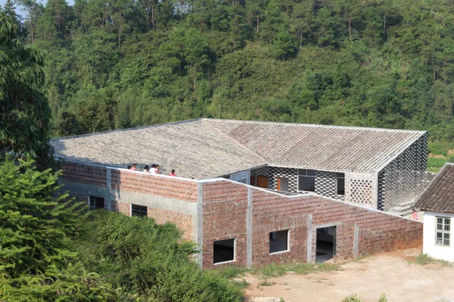 With this six-classroom addition to a primary school in Jiangxi Province, RUF produced a U-shaped structure with a courtyard open on one side. A continuous roof begins as a series of steps, providing 
