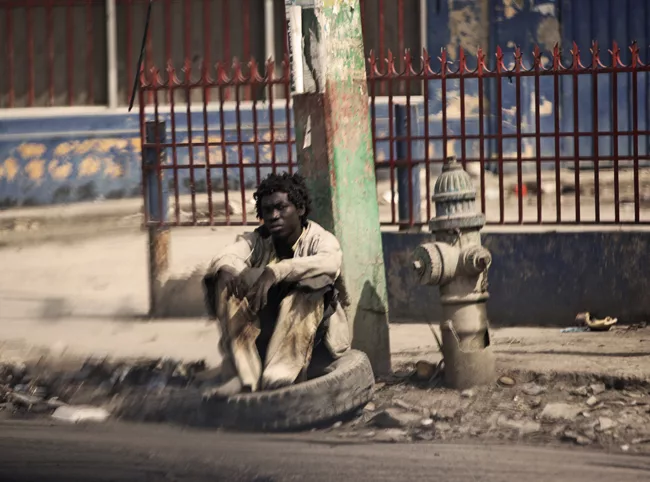 A man in tattered clothes rests on a tire in downtown Port-au-Prince. <em>January 2012</em>.