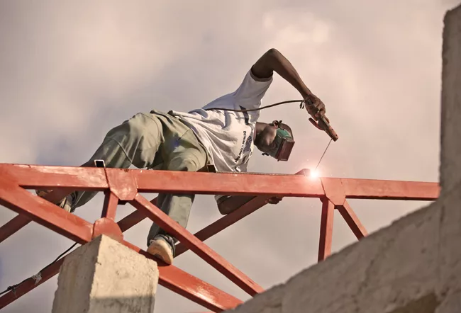 A man steadies himself as he welds a roof structure for a new school under construction in a rural area. <em>January 2012</em>.