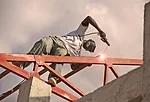 A man steadies himself as he welds a roof structure for a new school under construction in a rural area. <em>January 2012</em>.