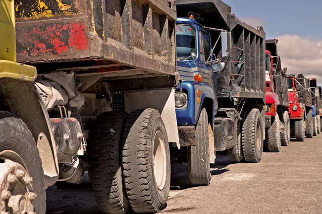 A line of trucks awaits entry into a mountainside quarry, where they will pick up material for mixing concrete. <em>January 2012</em>.