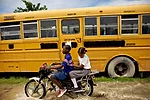 Kids navigate floodwaters on a small motorcycle, passing a yellow school bus. <em>April 2010</em>.