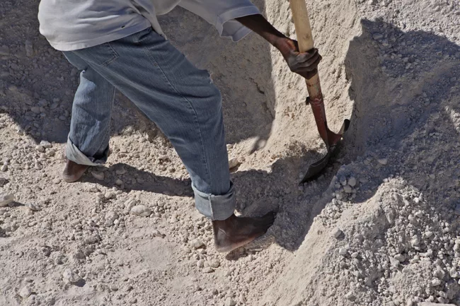 Shoeless men with bamboo-handled shovels fill the trucks, one by one. <em>January 2012</em>.