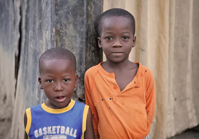 In Villa Rosa, an impoverished Port-au-Prince neighborhood, two boys stand outside of their home made of rusted metal and wood scraps. <em>January 2012</em>.