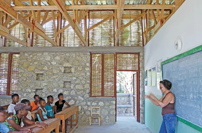 Openings covered with locally fabricated bamboo screens help ventilate the two-classroom building. Stones used for the foundation walls and entrance facade were collected from a nearby riverbed.