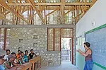 Openings covered with locally fabricated bamboo screens help ventilate the two-classroom building. Stones used for the foundation walls and entrance facade were collected from a nearby riverbed.