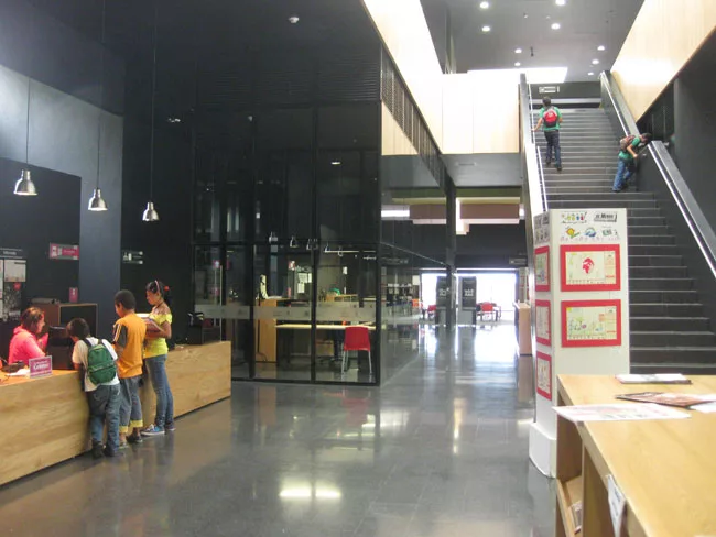 Next to the front desk, glass-walled offices bring transparency to administrative functions. The children's reading room is visible at the far end of the ground floor and a central stair leads to the