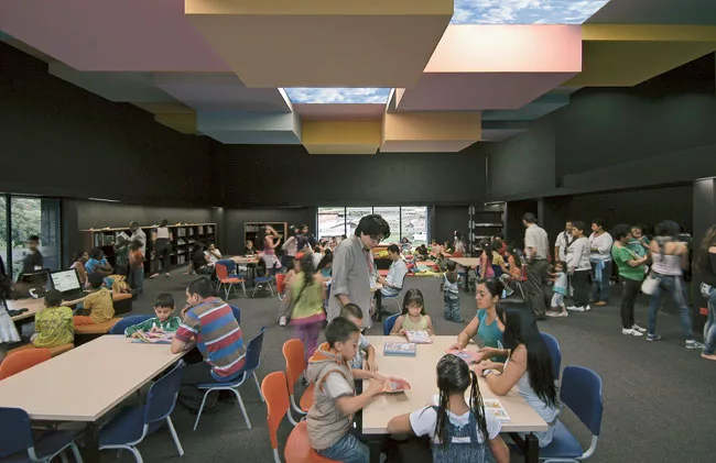 The children's reading room is animated by large windows, which admit light and the bustling activity outside, as well as a playful ceiling, illuminated by light fixtures with a sky motif. The design