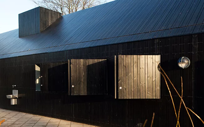 Black from charring, the wood cladding is mounted on the exterior of the existing building in an alternating pattern of three plank widths. It is heat modified to strengthen the wood.
