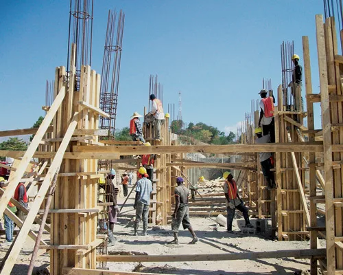 Haitian workers are learning U.S.-style construction, tempered by budget and supply-chain realities. The design, donated by Nicholas Clark Architects, uses natural ventilation and solar power to count