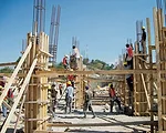 Haitian workers are learning U.S.-style construction, tempered by budget and supply-chain realities. The design, donated by Nicholas Clark Architects, uses natural ventilation and solar power to count