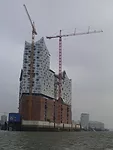 The Elbphilharmonie Concert Hall features a former cocoa warehouse crowned with a curved glass structure. The project has been plagued with cost overruns and construction difficulties; the estimated c