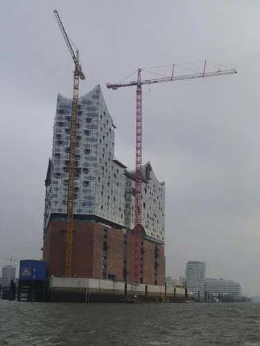 The Elbphilharmonie Concert Hall features a former cocoa warehouse crowned with a curved glass structure. The project has been plagued with cost overruns and construction difficulties; the estimated c