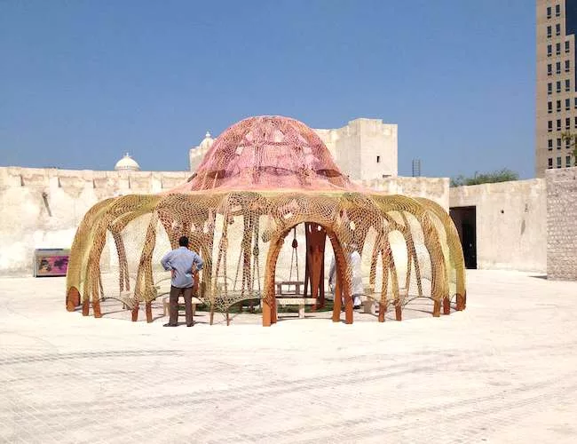 A tent made from a nest of red and orange polyester cable, <em>Enquant a cultural nos separa, a natureza nos une [While Culture Moves Us Apart Nature Brings Us Together]</em>, 2013, by Brazilian artis