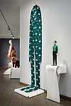 A stretched men’s suit by John Bartlett, based on a late 19th century wood statue, evokes both Joseph Beuys and a car dealership’s windsock. Yeohlee Teng’s paper dress is in the back
